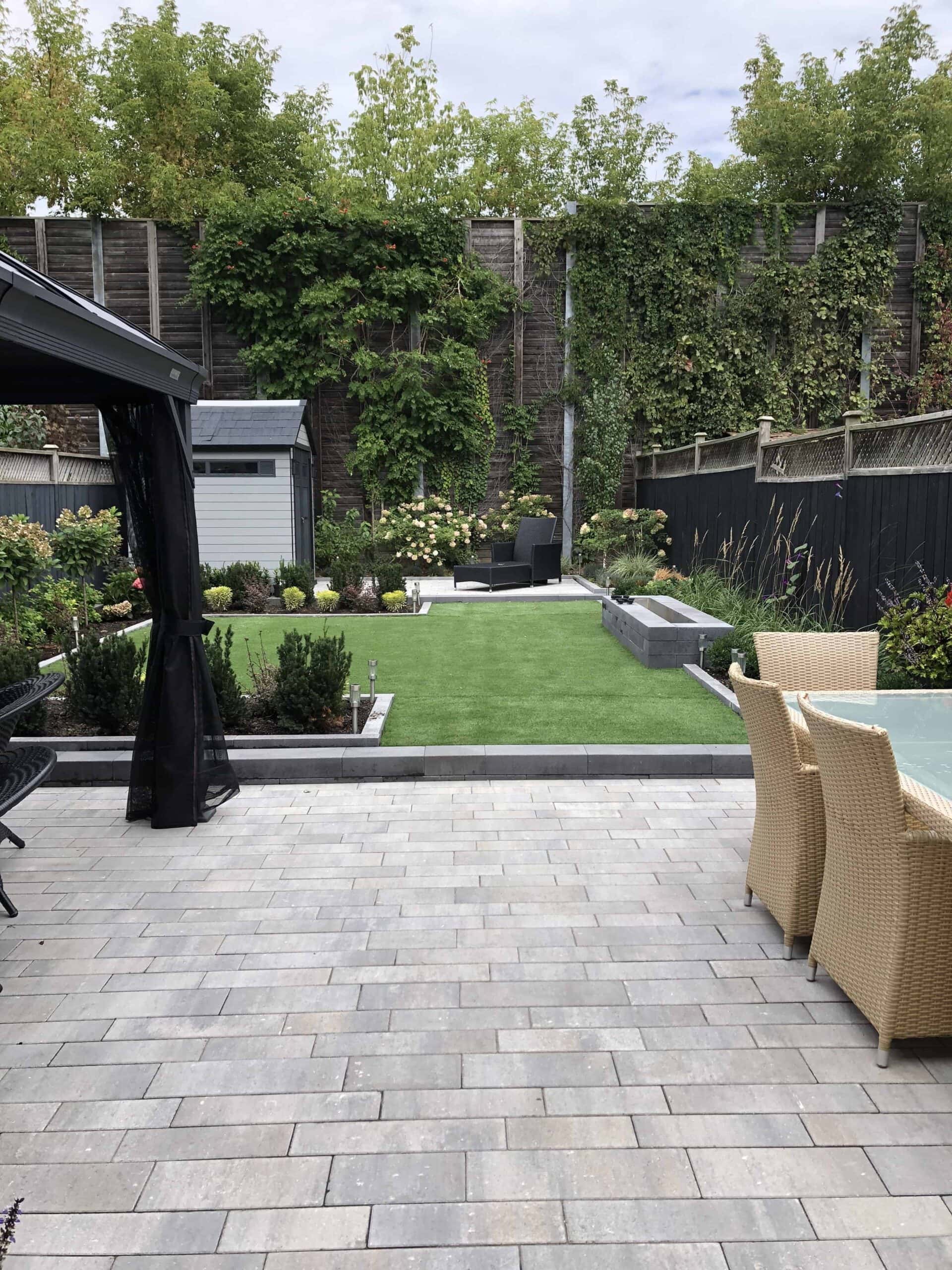 Backyard living space, featuring a stone patio that leads into a landscaped grass area