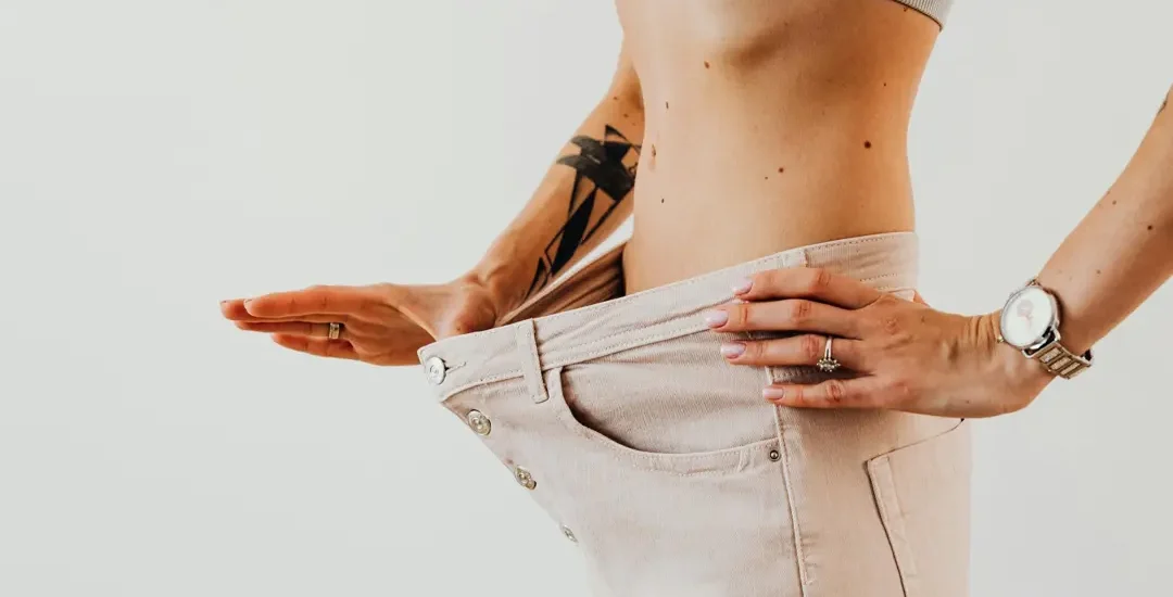 Resultado de como emagrecer: mulher mostra calça larga após perda de peso significativa.