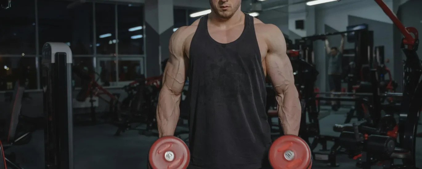 "Homem musculoso fazendo exercício de bíceps com halteres na academia, focado no treino de hipertrofia"