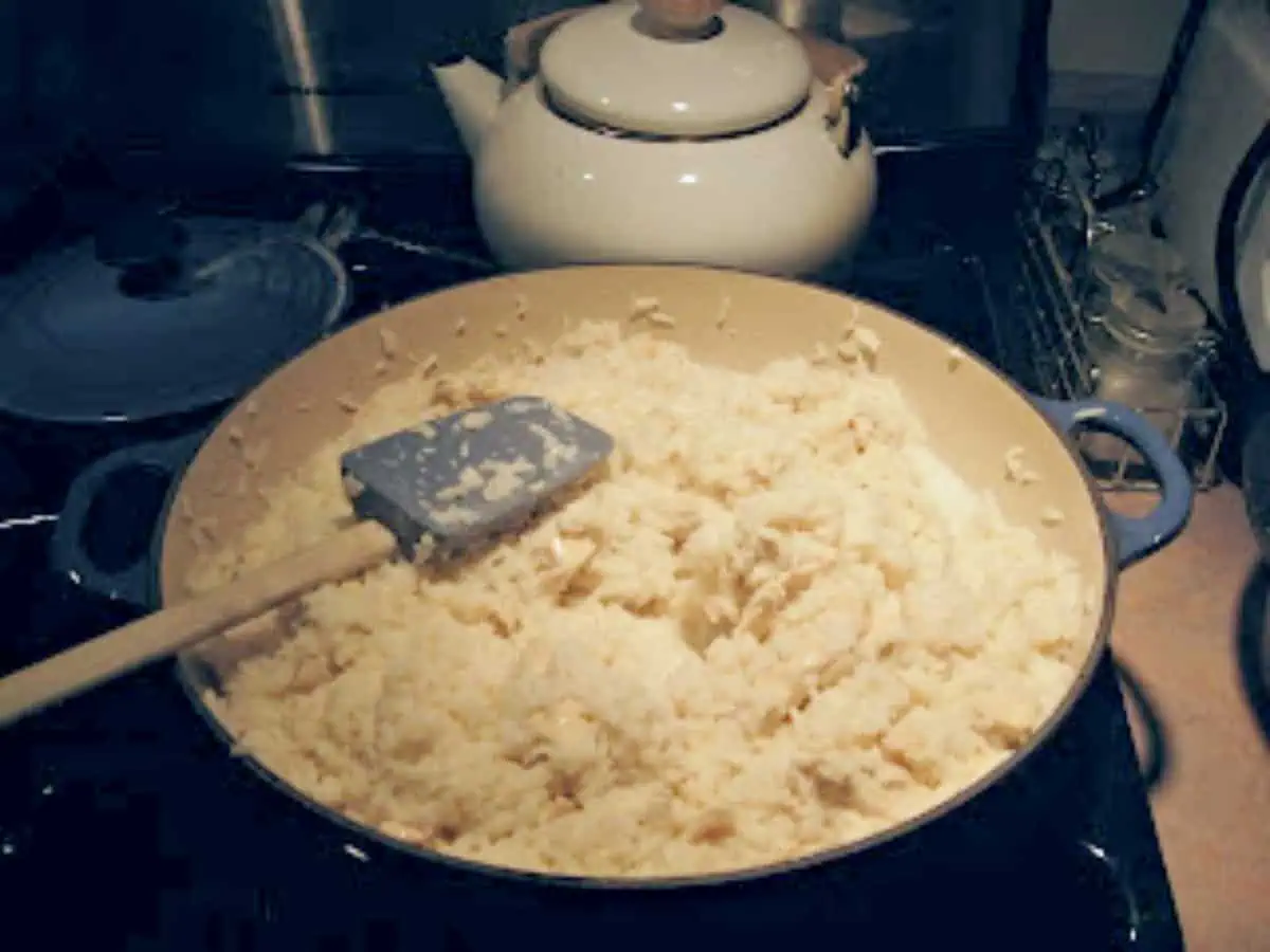 Skillet of chicken and rice mixed with milk on a stove.