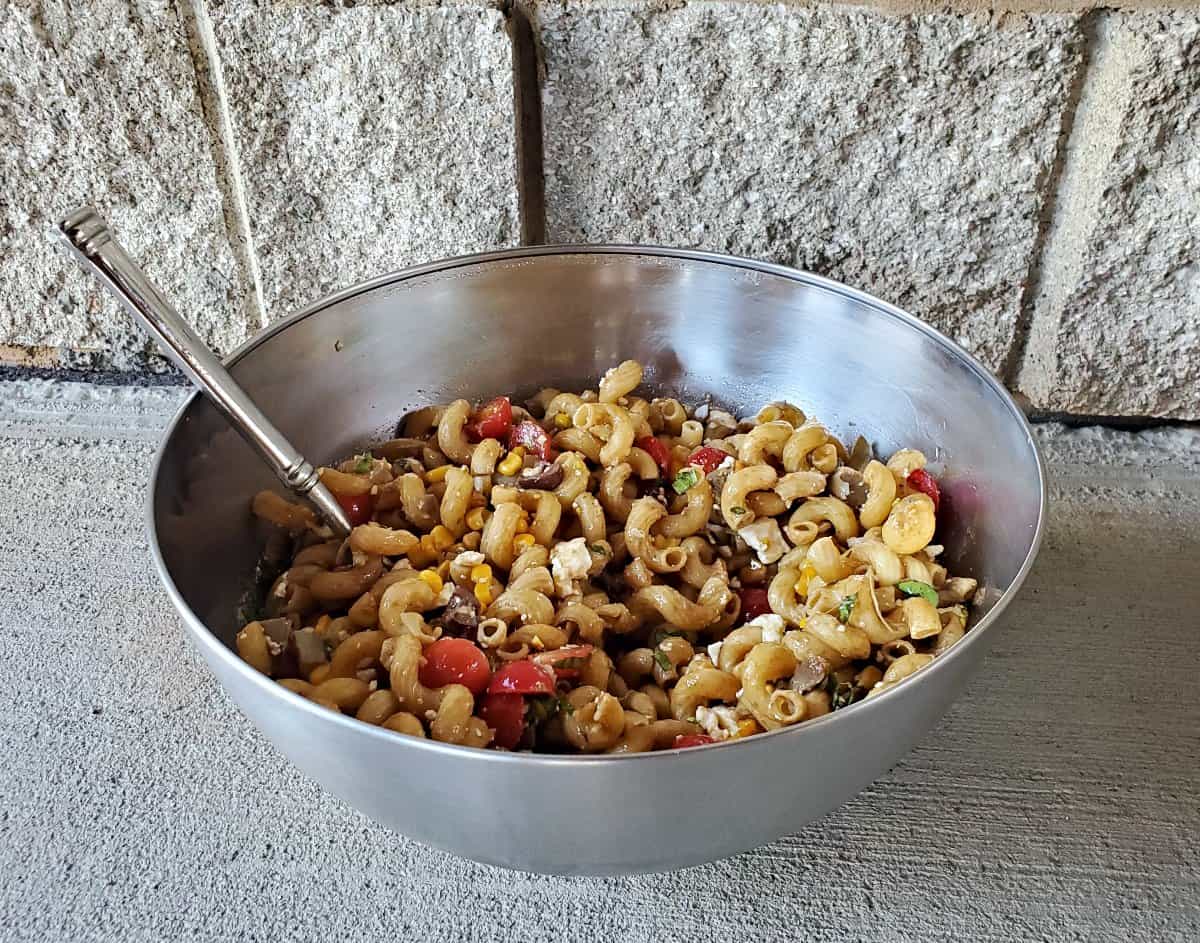 Big silver bowl of veggie pasta salad in front of a stone wall.
