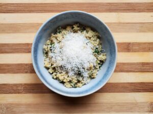 Bowl of spinach quinoa topped with parmesan cheese on a striped wooden board