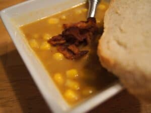Image shows potato corn chowder in a bowl topped with bacon bits.