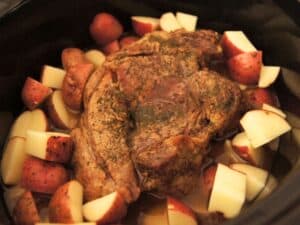 Image shows red potatoes added to the ingredients of pot roast in the crock pot.