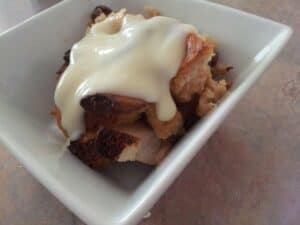 Image shows homemade bread pudding with custard sauce.