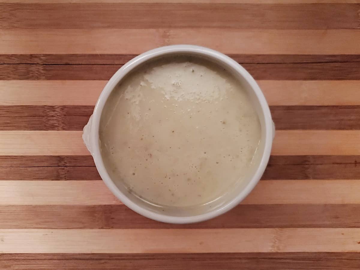 Overhead view of a bowl of homemade cream of celery soup on a wooden board.