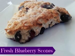 White plate with a fresh blueberry scone sitting on it.