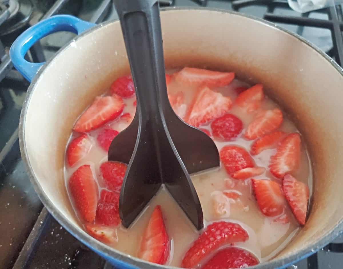 Mashing fresh strawberries in a blue pot.