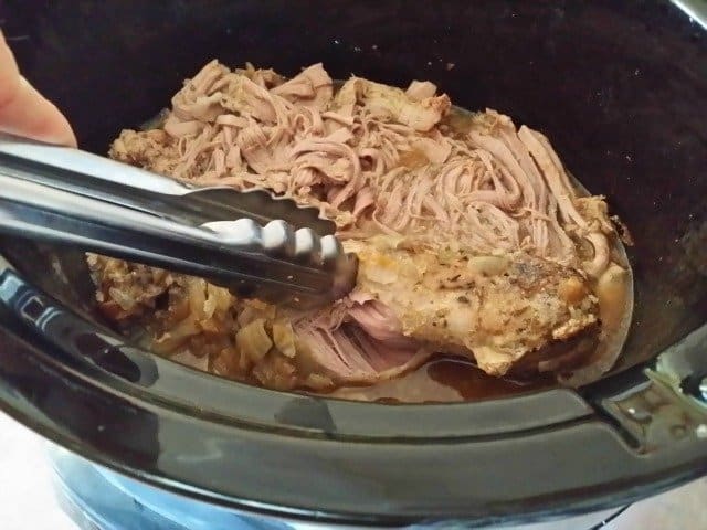 Using tongs to shred pork
