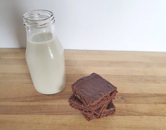 Sheetcake brownies stacked three high and a jug of milk on a wooden board.