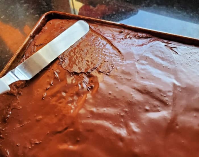 Spreading chocolate frosting on Texas sheetcake brownies with an offset spatula.