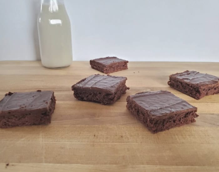 Five Texas sheetcake brownies on a wooden board with a jug of milk.