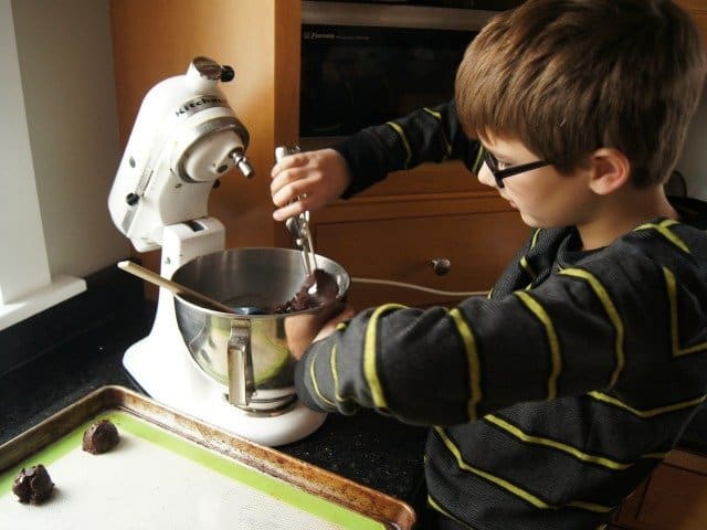 Boy scooping chocolate cookie dough from a stand mixer.
