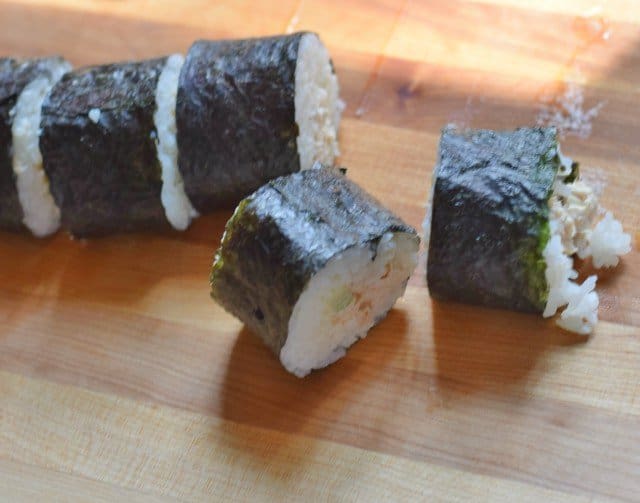 Slice homemade spicy tuna rolls with wet serrated knife