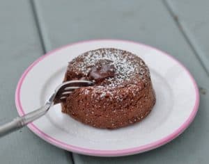 Fork cutting into a molten chocolate cake on a small white plate.