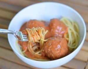 Image shows a bowl of spaghetti and meatballs with a fork twirling the spaghetti.