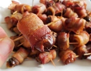 https://instagram.com/HonestAndTruly a hand holding a Homemade bacon wrapped date with more behind it.