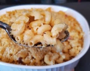 Image shows a Scoop of bacon mac and cheese with the entire casserole behind it.