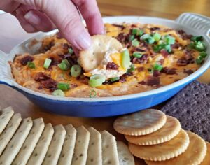 Dipping a cracker into hot bacon cheddar dip