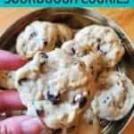Holding a cookie over a tin of other cookies.