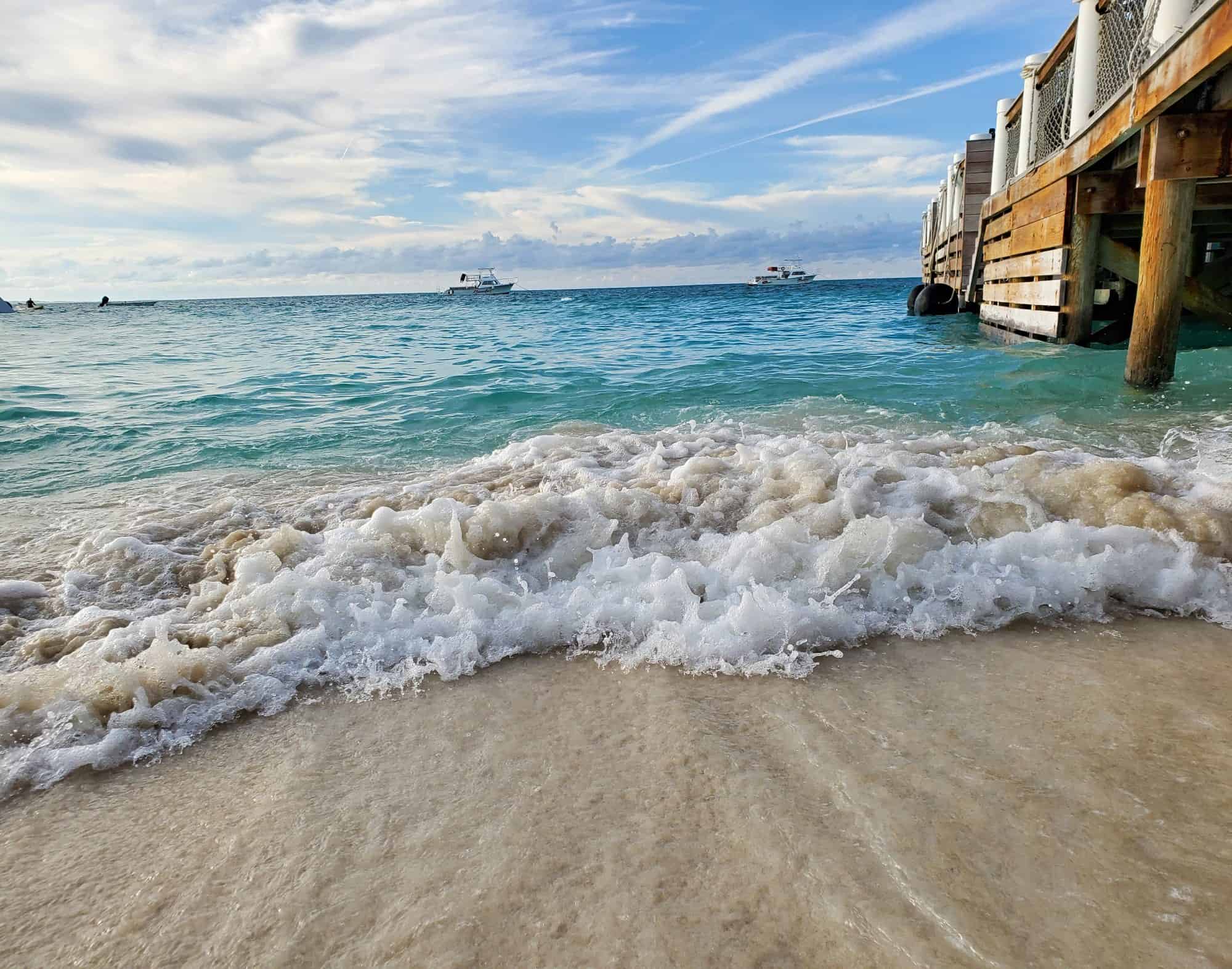 Waves crash on the beach next to a wooden pier.