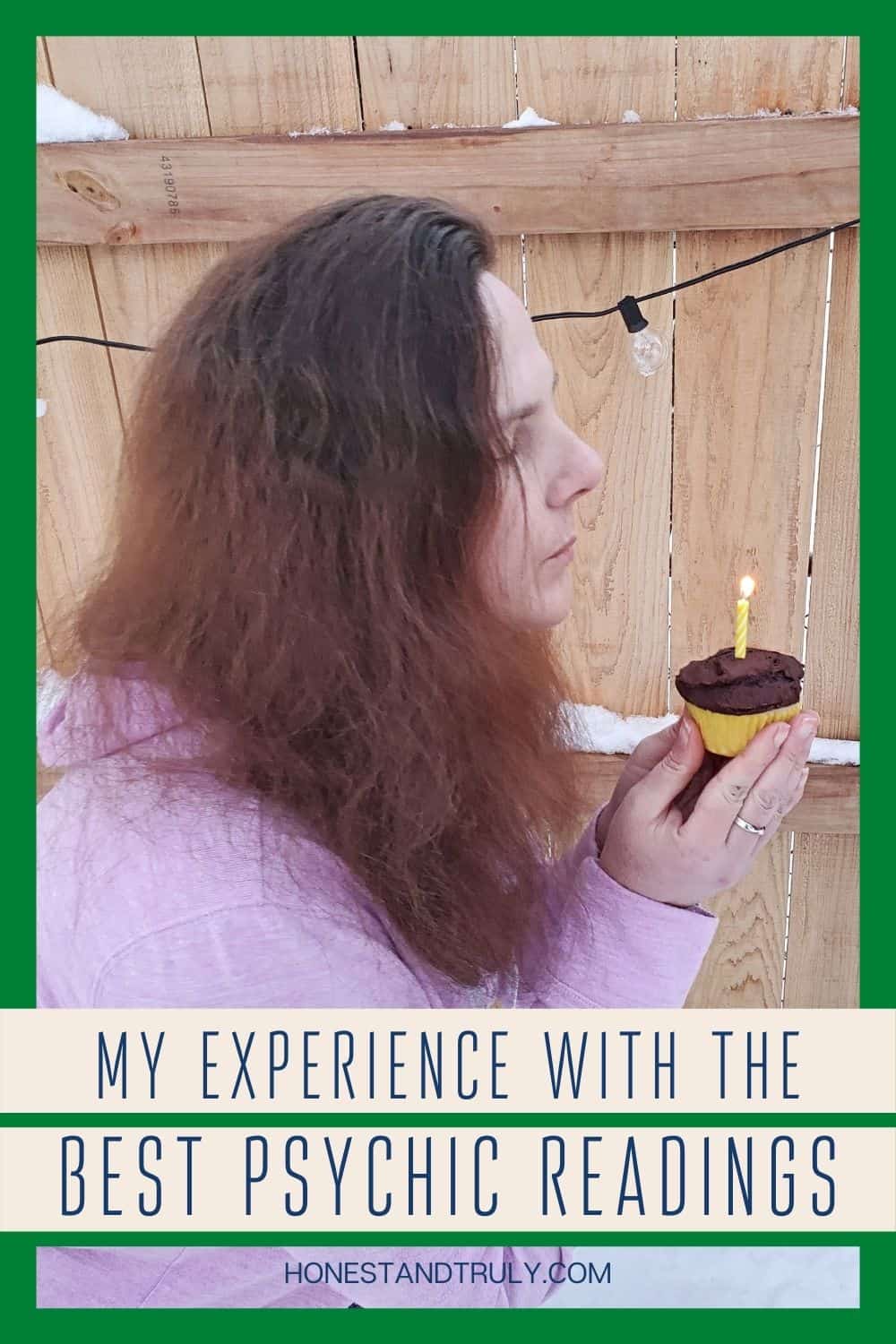 Outside blowing out a candle on a cupcake by a wooden fence.