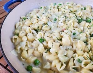 Closeup of a pot of pasta with peas and fresh dill.