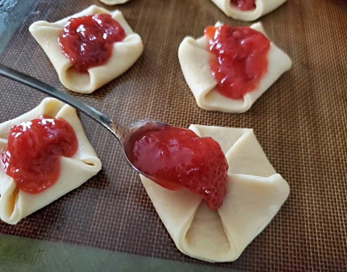 Adding a spoon of strawberry filling to dough pinwheel.