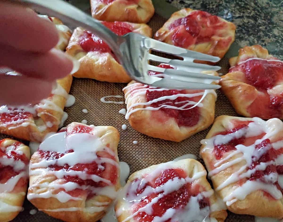 Drizzling strawberry danishes with icing.