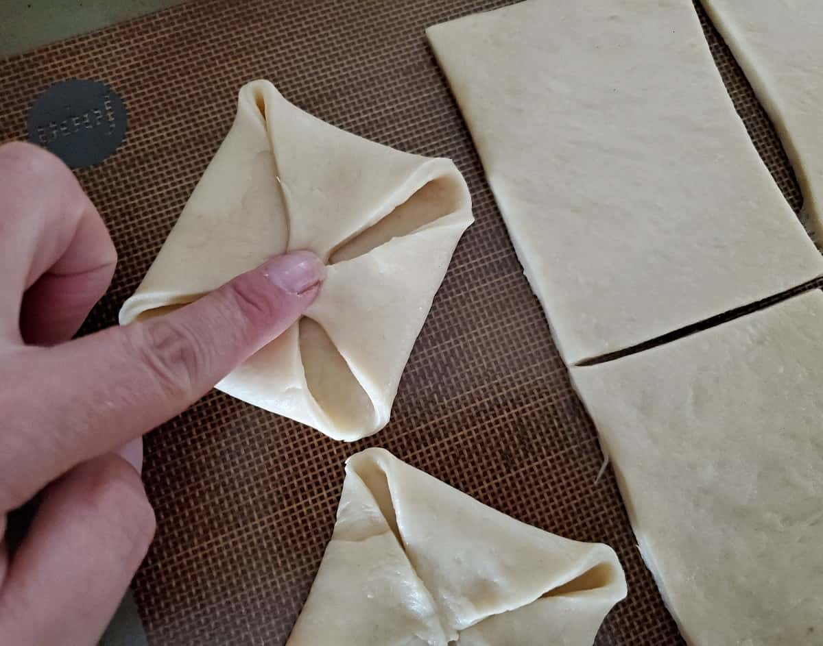 Finger pressing dough corners into center to form a pinwheel shape.
