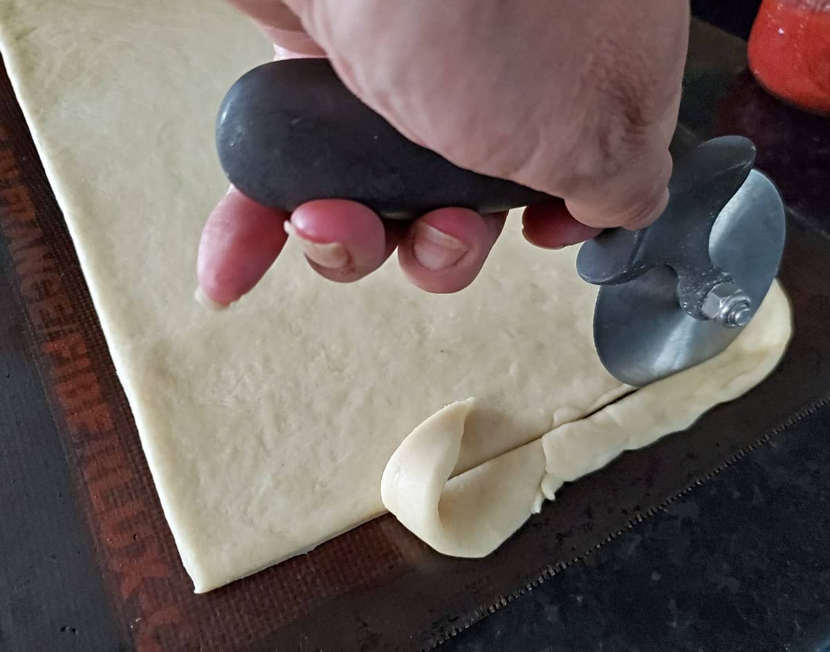 Using a pizza peel to trim edge from dough to make a straight line.