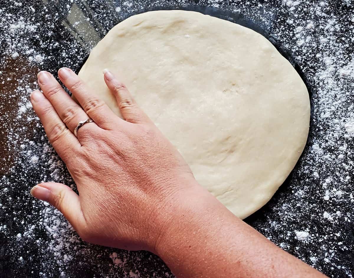 Flattening dough by hand on a floured surface.