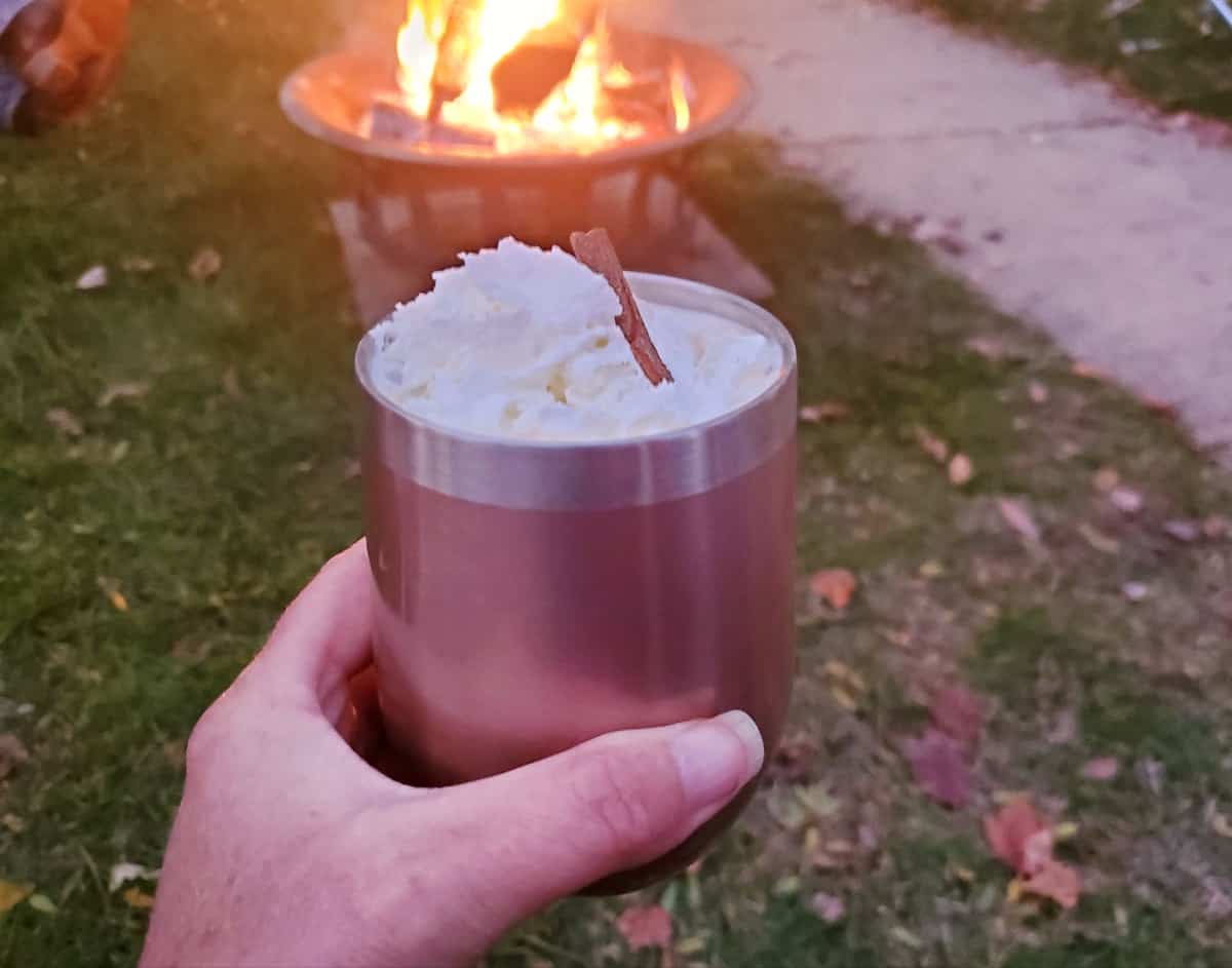 Holding a hot apple cider in front of a fire.