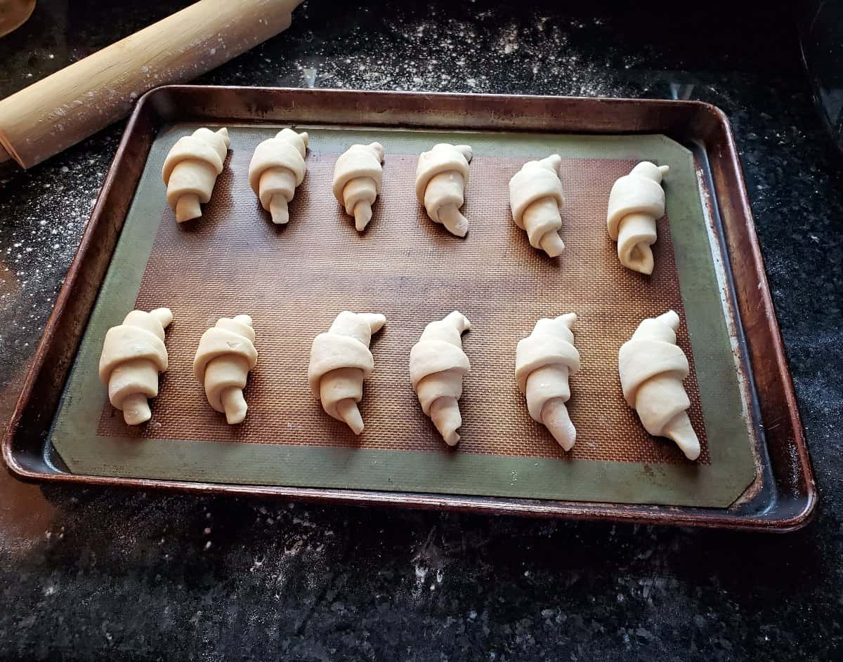 Homemade crescent rolls on a baking pan ready to rise.