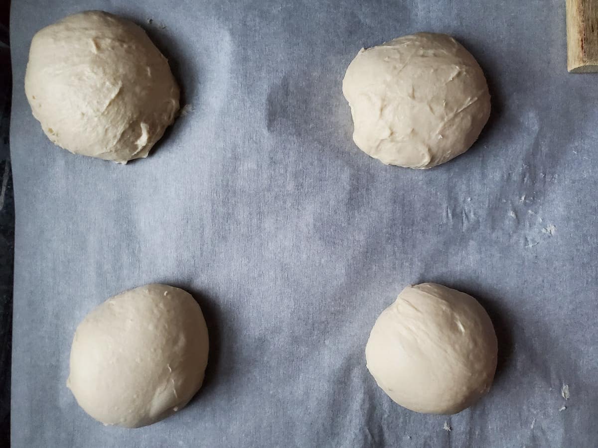 4 bread dough balls on parchment paper ready to rise,
