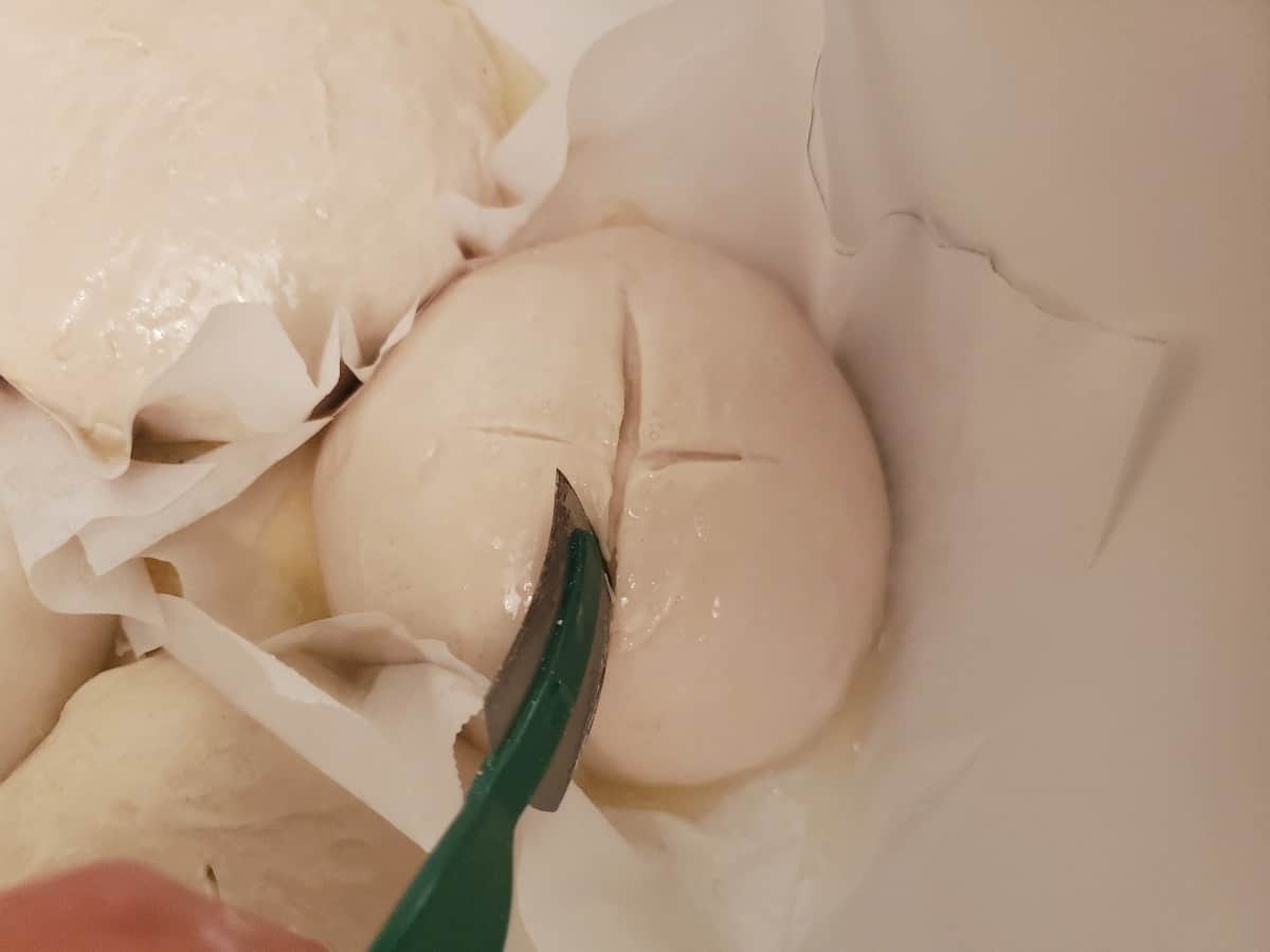 A lame tool cutting a cross on a round of bread dough,