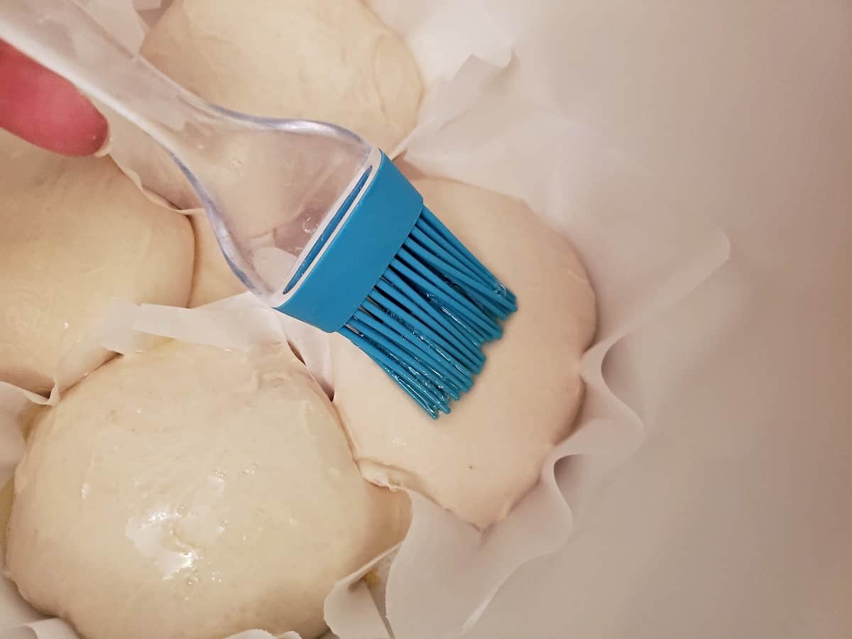 Brushing dough balls with egg wash using a blue pastry brush,