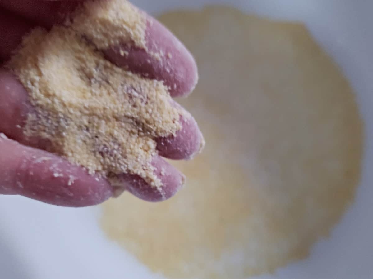 Cornmeal on fingers with a white pot under it lined in cornmeal.