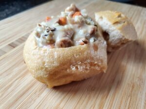 Sourdough bread bowl with chicken soup on a wooden board.