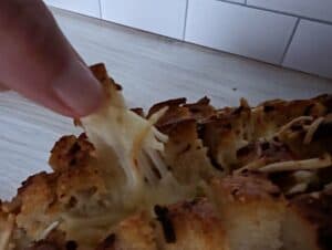 Hand pulling off a piece of cheesy garlic pull apart bread.