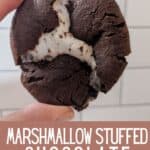 Hand holding a chocolate cookie in front of a subway tile backsplash with text marshmallow stuffed chocolate cookies.
