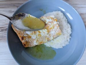 Spoon drizzling orange glaze on salmon with rice on a blue plate.