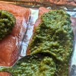 Image shows a spoon Adding pesto to salmon with text oven baked pesto salmon.