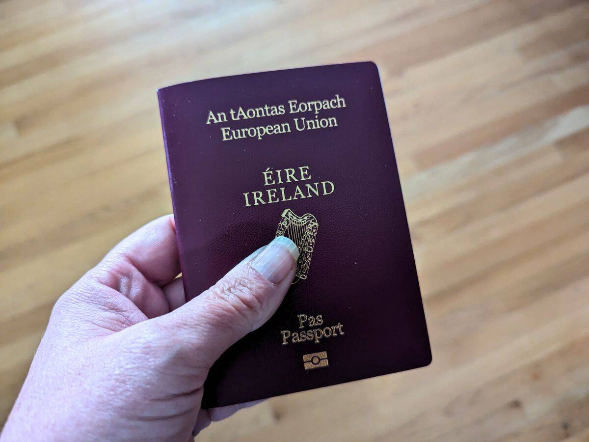 Image shows a Hand holding an irish passport over a wooden floor.