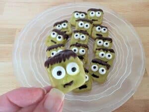 Image shows a Hand holding pretzel Frankenstein over a plate with more.