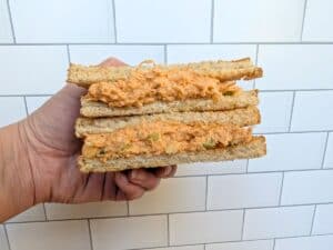 Image shows a hand holding a buffalo chicken salad sandwich against a white background.