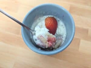Image shows a spoonful of strawberry mug cake showing its soft, fluffy texture with visible strawberry pieces.