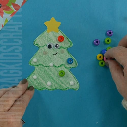 A completed Christmas tree craft made with green paper, colorful beads, pipe cleaners, and a star topper, perfect as an easy craft for kids and a festive Christmas tree craft.  step 6 adding the ornaments to the christmas tree 
