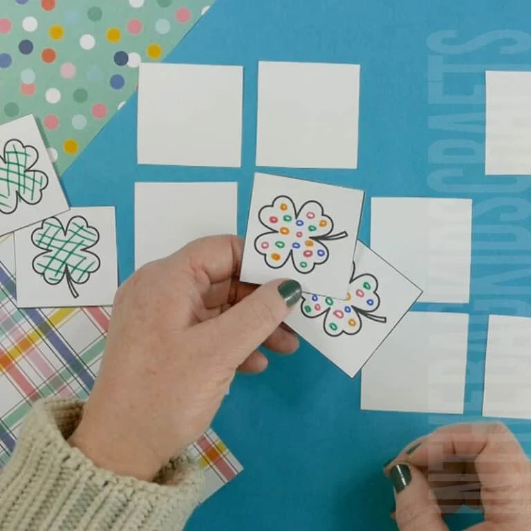 A pair of hands cutting out decorated clover cards from a free printable sheet, creating a fun memory game as a St. Patrick's Day activity for kids.