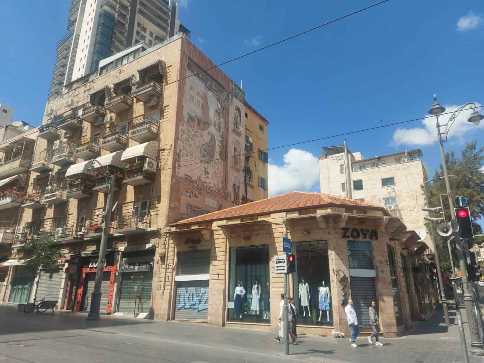 ציור הקיר האייקוני ברחוב יפו, סמוך לשוק מחנה יהודה בירושלים, תחת שמיים כחולים, על רקע חנויות סגורות